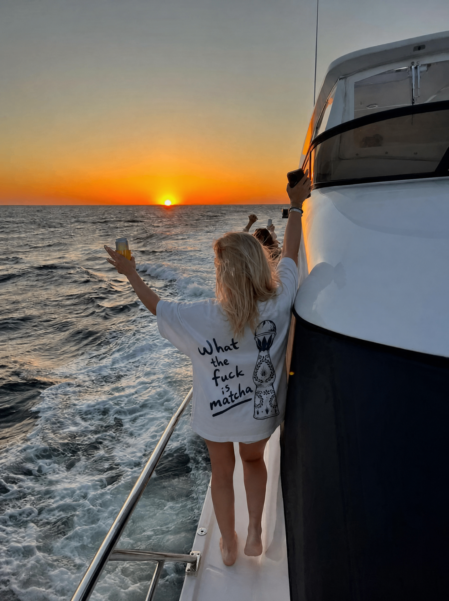 Guest in the What the Fuck Is Matcha tee cheering at sunset from the back of a yacht