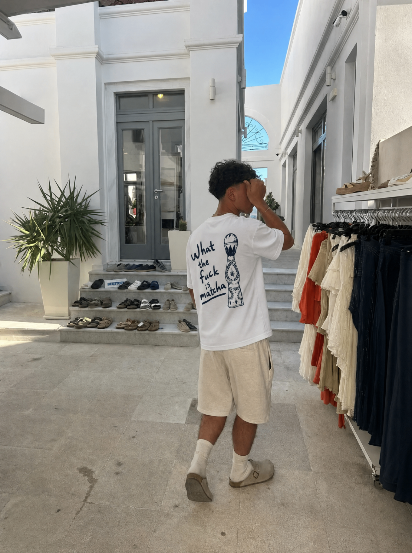 Guest in the What the Fuck Is Matcha tee outside a whitewashed boutique in Mykonos